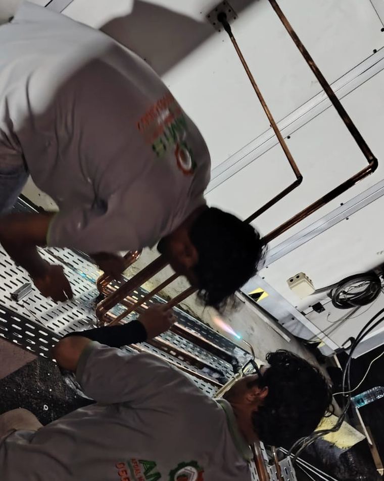Two AMTS technicians installing copper piping above a ceiling void
